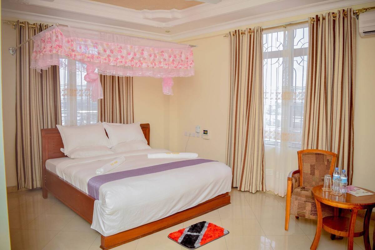 A hotel room with a bed, curtains, a chair, a table, and a window.