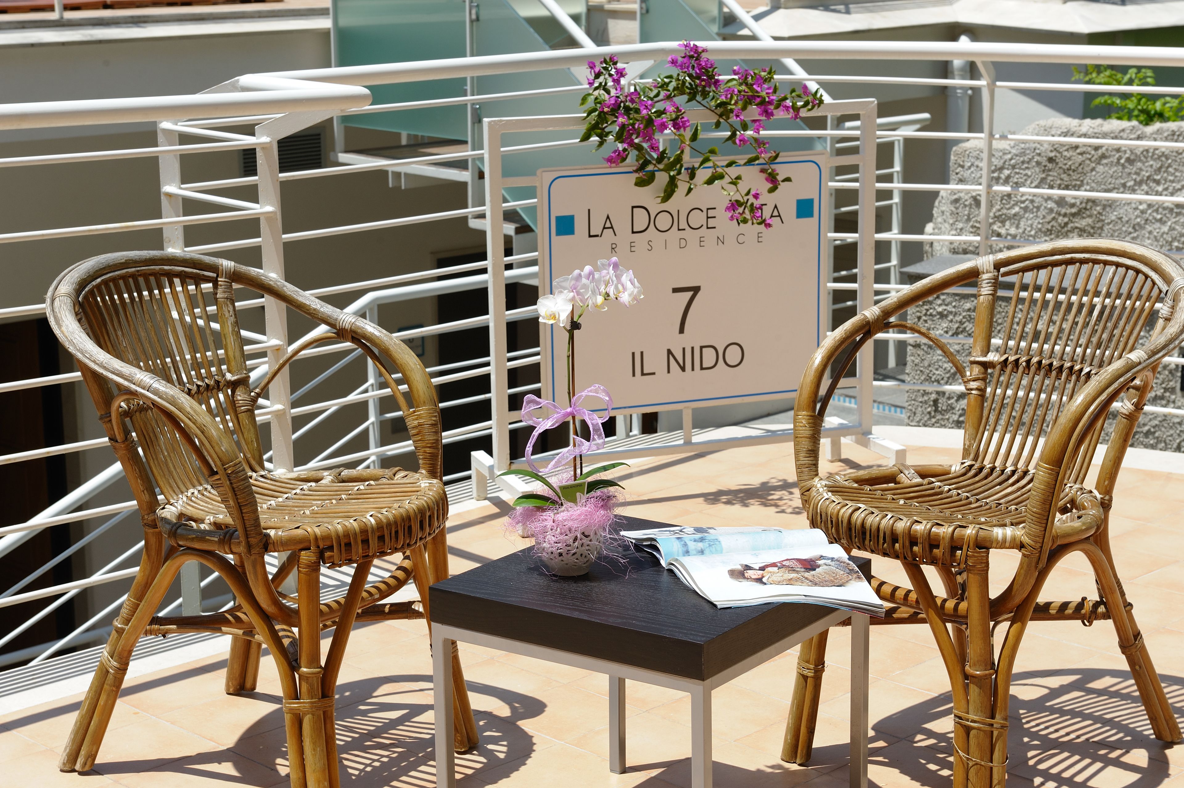 Dos sillas de mimbre, una mesita y un cartel con la inscripción 'La Dolce Vita Residence 7 Il Nido'.