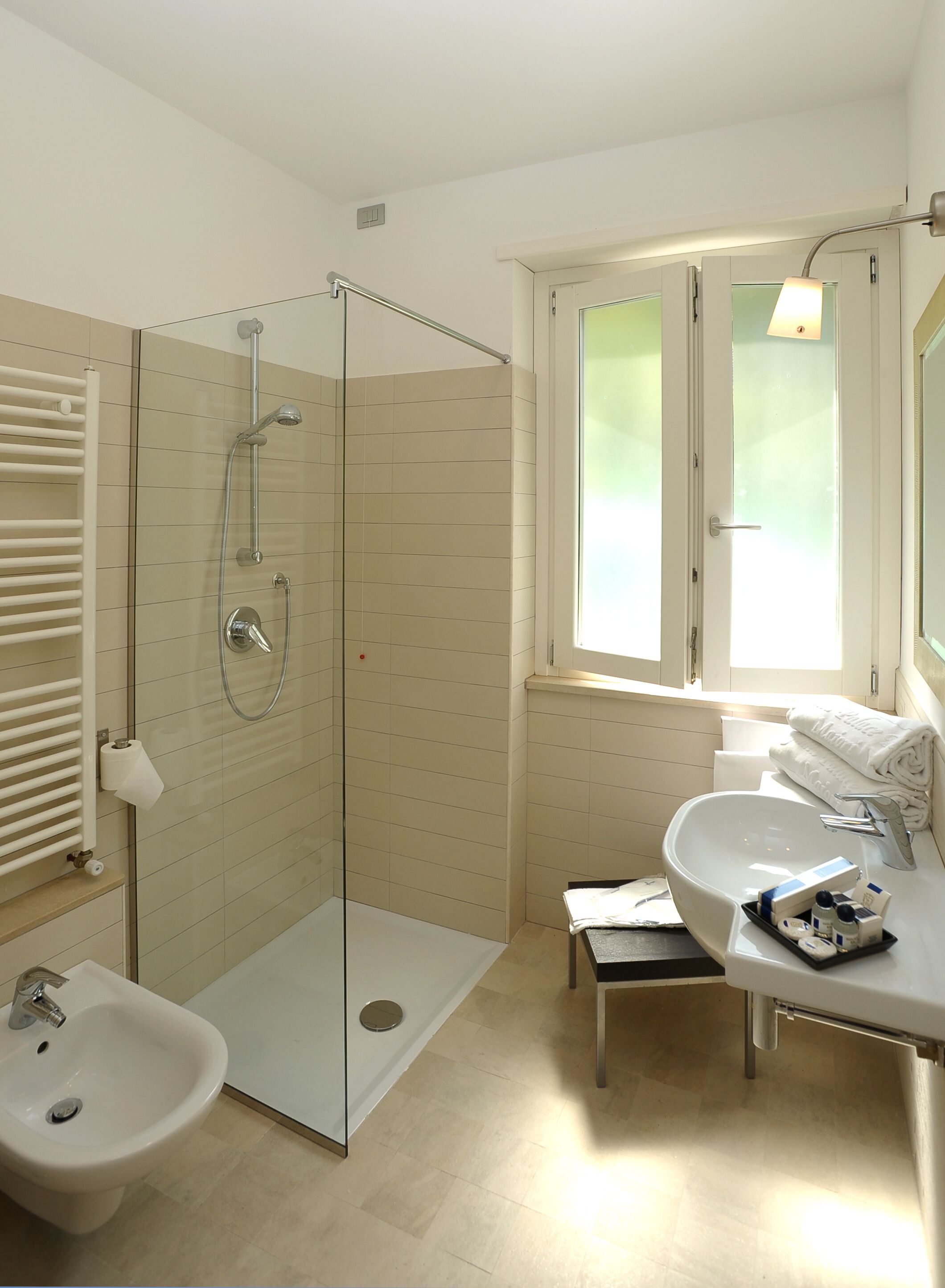 Un baño moderno con ducha de vidrio, un bidé, un lavamanos y una ventana que proporciona luz natural.