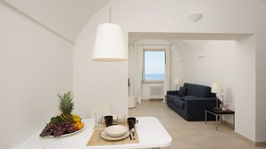 Ein modernes, minimalistisches Zimmer mit einem für zwei Personen gedecktem Esstisch, einem dunkelblauen Sofa und Meerblick durch ein großes Fenster.