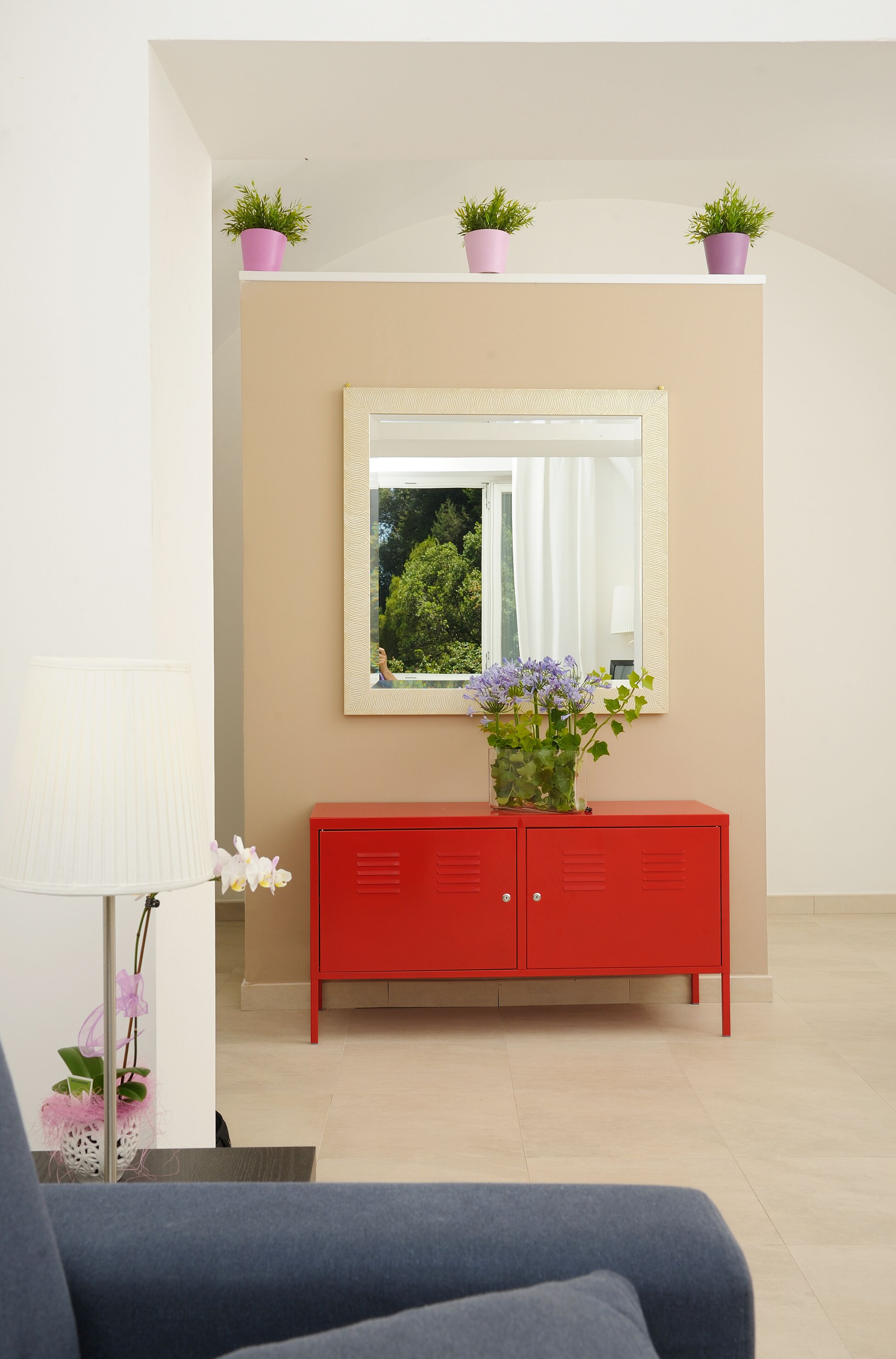 Una habitación con un armario rojo, un espejo y plantas en macetas sobre una estantería.