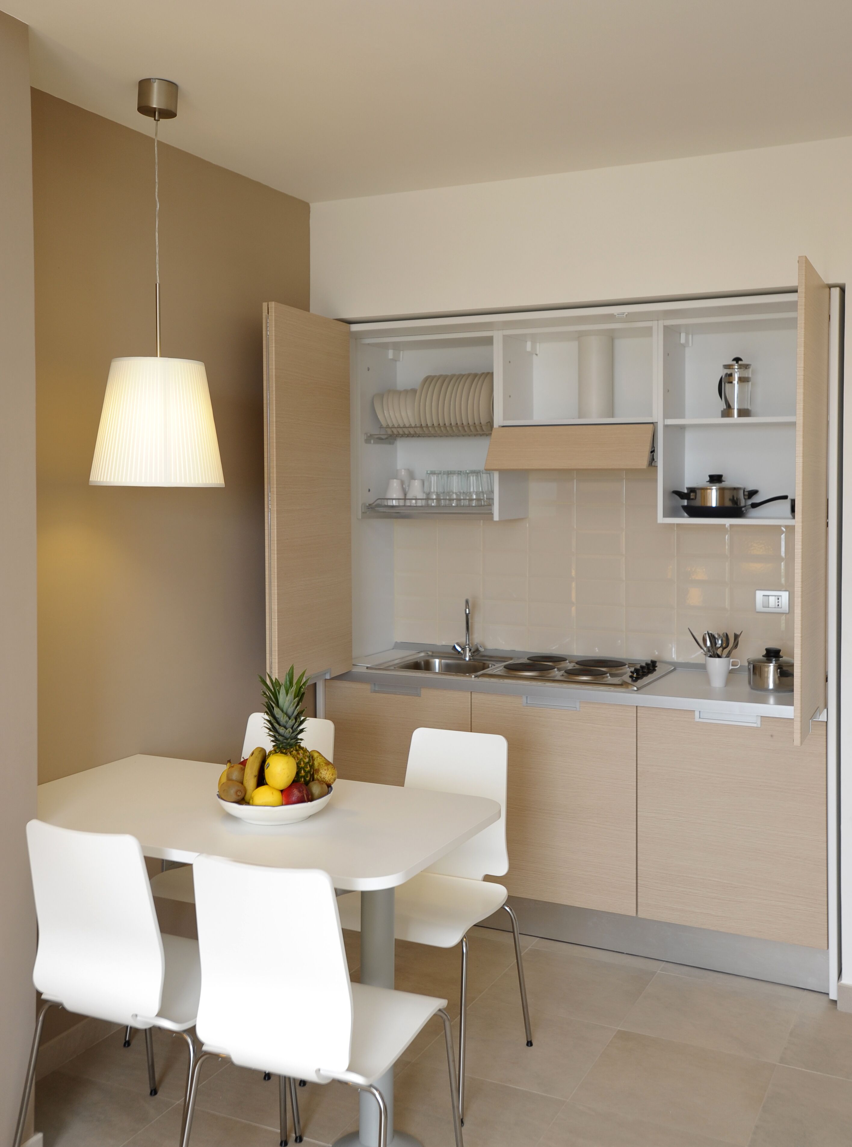 Una cocina moderna con armarios blancos, una mesa de comedor con sillas y un frutero.