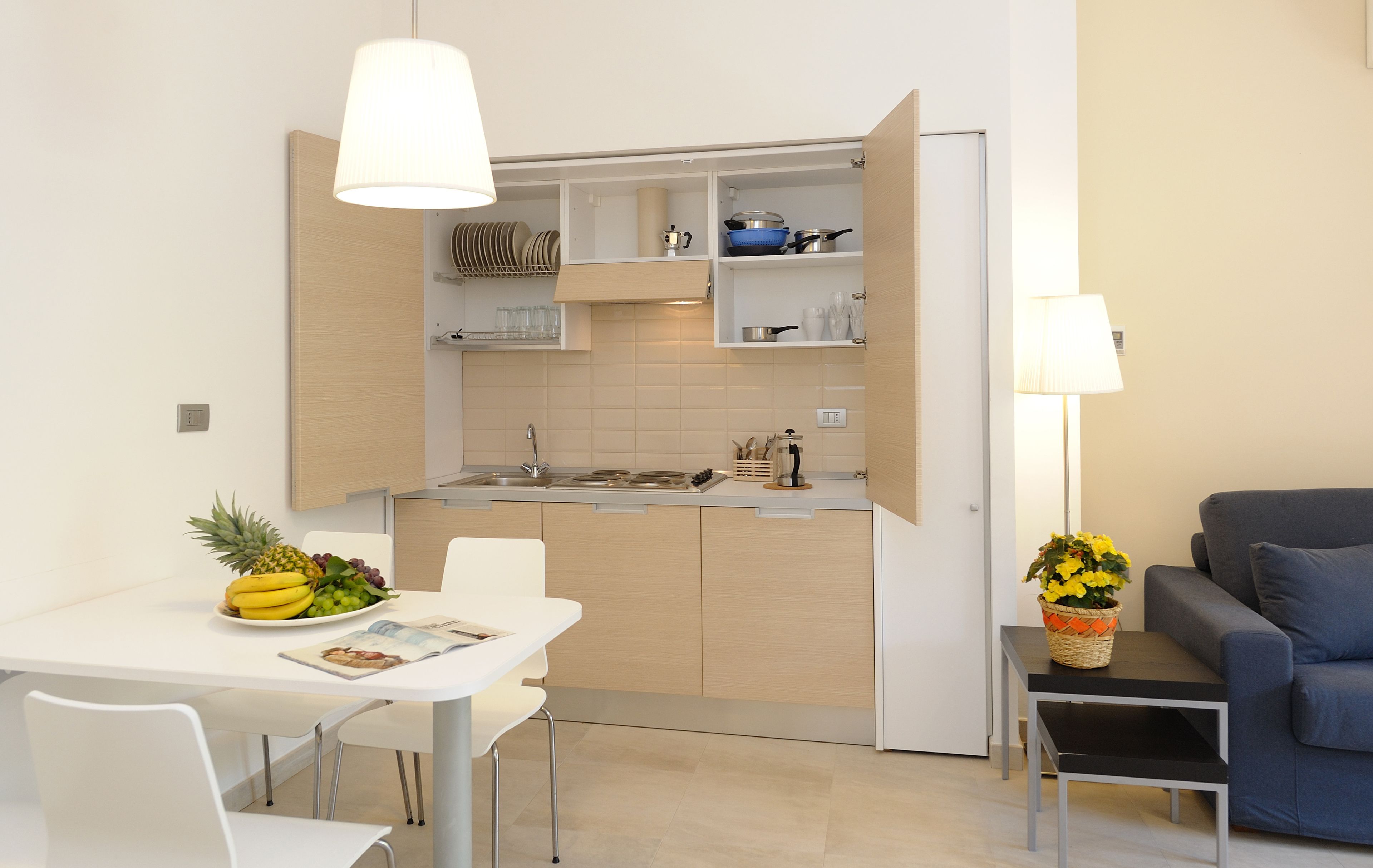 A modern kitchen with an open layout, a dining table with chairs, and a small seating area with a sofa and a lamp.