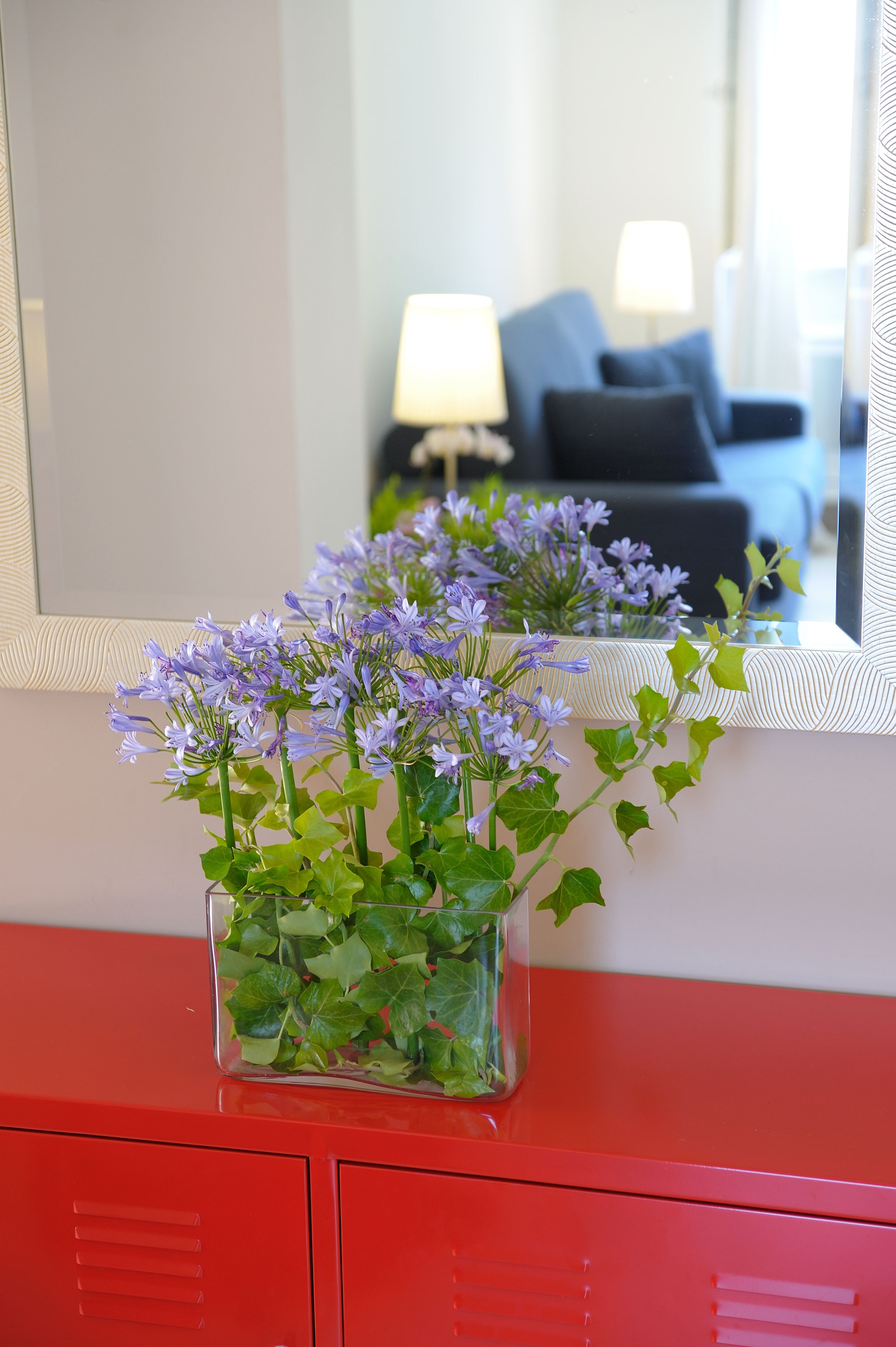 Um armário vermelho com um vaso de vidro contendo flores roxas.