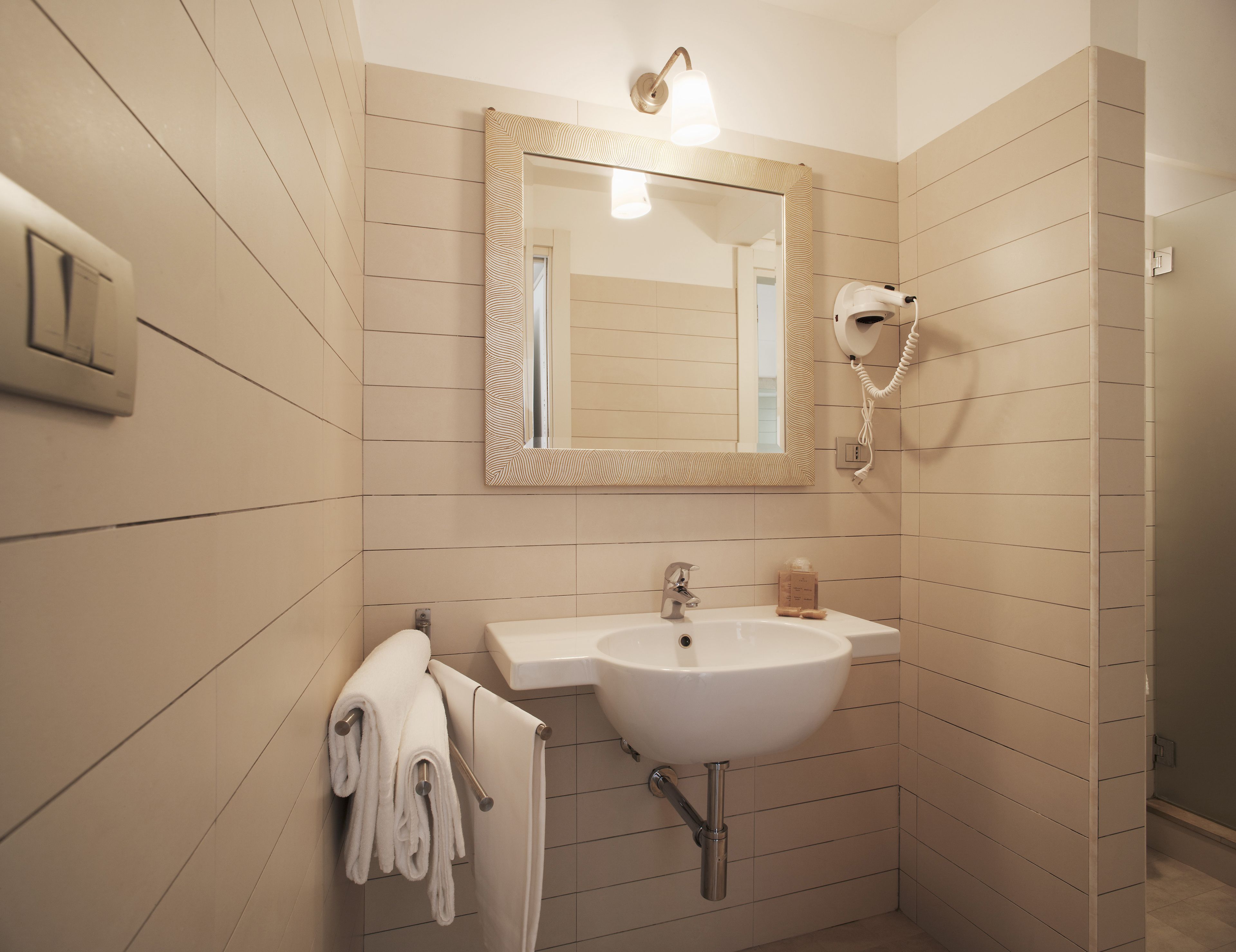 A bathroom with a sink, mirror, towel rack, and a hairdryer on the wall.