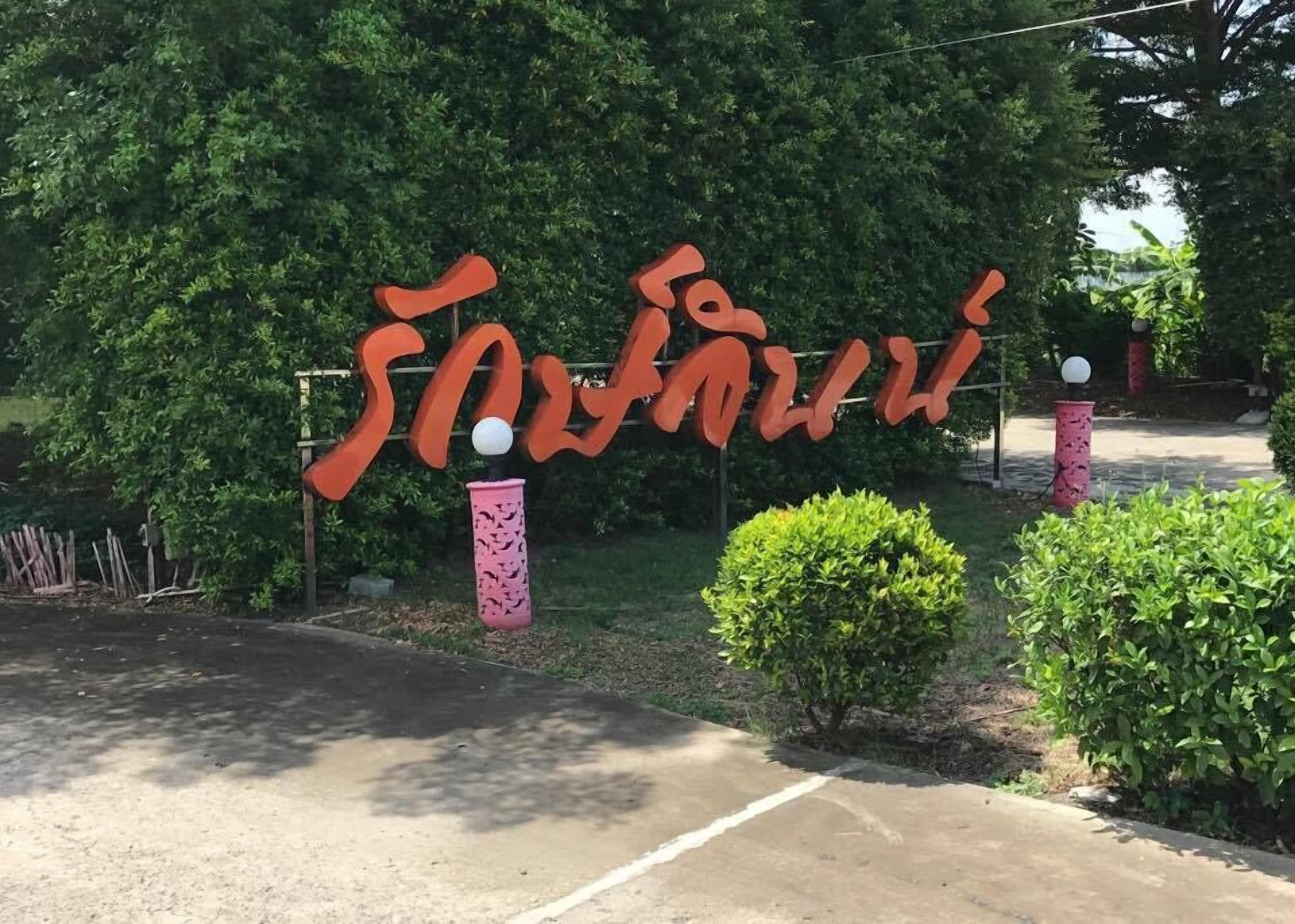 A sign with large, stylized letters in a foreign script, surrounded by greenery and a paved area.