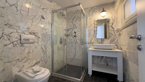 A bathroom with a glass-enclosed shower, a toilet, and a vanity with a sink and mirror. - Buyukada Port Hotel (Adalar)