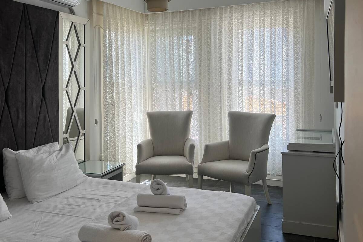A modern hotel room with a large bed, two armchairs, a desk, and a TV.