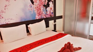A hotel room with a bed, white bedding, a red decorative pillow, and a large floral artwork on the wall. - Tonrak Resort (Ongkharak)