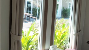 A room with large windows, a white table, two pink ottomans, and a white mug on the table. - Tonrak Resort (Ongkharak)