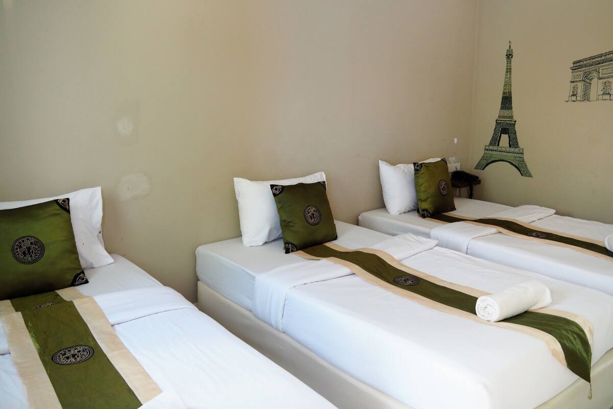 A hotel room with three single beds, each with white bedding and green decorative pillows.