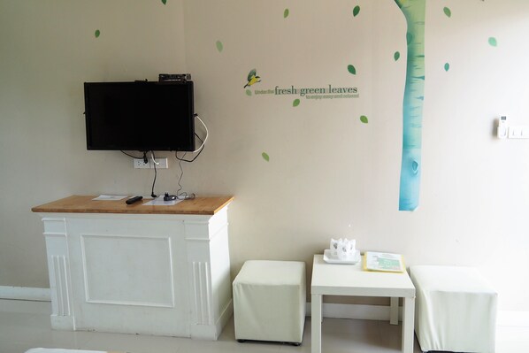 Una habitación con una televisión montada en un mueble blanco, una mesita con una bandeja y un adhesivo mural de un árbol y hojas.