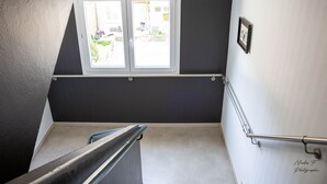 Una escalera con barandilla de metal, una ventana con vistas al exterior y una puerta con manija.