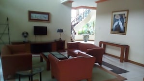 Una sala de estar con sofá, sillones, una mesa de centro, televisor y una escalera que sube a un nivel superior.