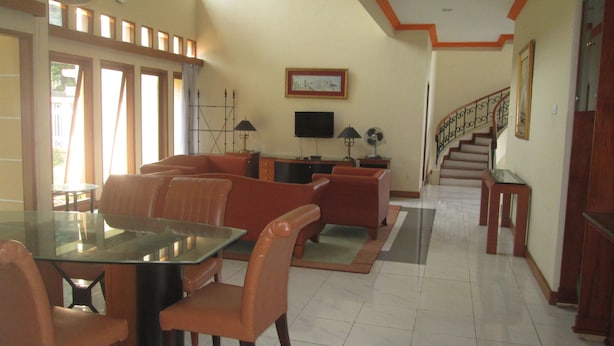 Amplia sala de estar con una mesa de comedor de vidrio, sofás de cuero, un televisor de pantalla plana y una escalera que conduce a otro nivel.