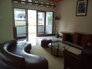 A living room with a glass coffee table, leather sofas, a wooden cabinet, and a potted plant. - Simply Homy Guesthouse Graha Puspa (Parongpong)