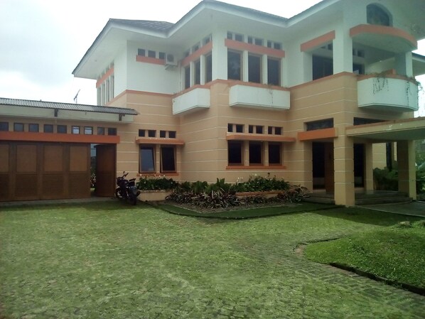 A two-story building with a flat roof, a covered entrance, and a small garden area with plants and a parked motorcycle.