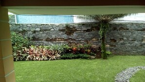 Un patio con pared de piedra, césped verde y diversas plantas.