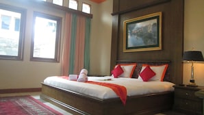 Habitación de hotel con una cama grande, un cuadro en la pared, una lámpara y una ventana con cortinas.