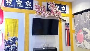 Una sala de estar moderna con un televisor de pantalla plana montado en una pared amarillo y blanco, un refrigerador pequeño blanco y un cubo de basura rosa.