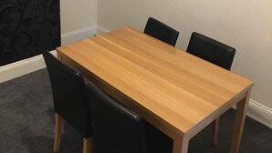 A small dining table with four chairs, a dark patterned wallpaper on one wall, and a plain white wall on the other. - Icon Gorleston Apartment (Great Yarmouth)