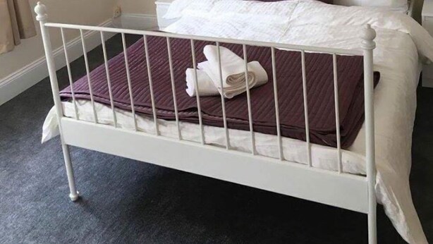 A neatly made bed with white linens and a purple blanket, a white metal headboard, a purple pillow, and a wall-mounted flower painting. - Icon Gorleston Apartment (Great Yarmouth)