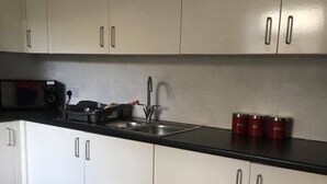 A modern kitchen with white cabinets, a black countertop, a microwave, a stove, and a sink. - Icon Gorleston Apartment (Great Yarmouth)