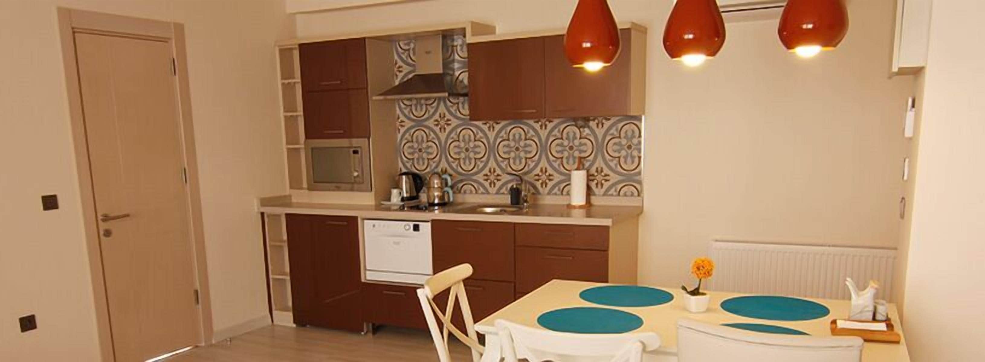 A compact kitchen with a microwave, stove, and sink, a dining area with a table and chairs, and a door leading to another room.