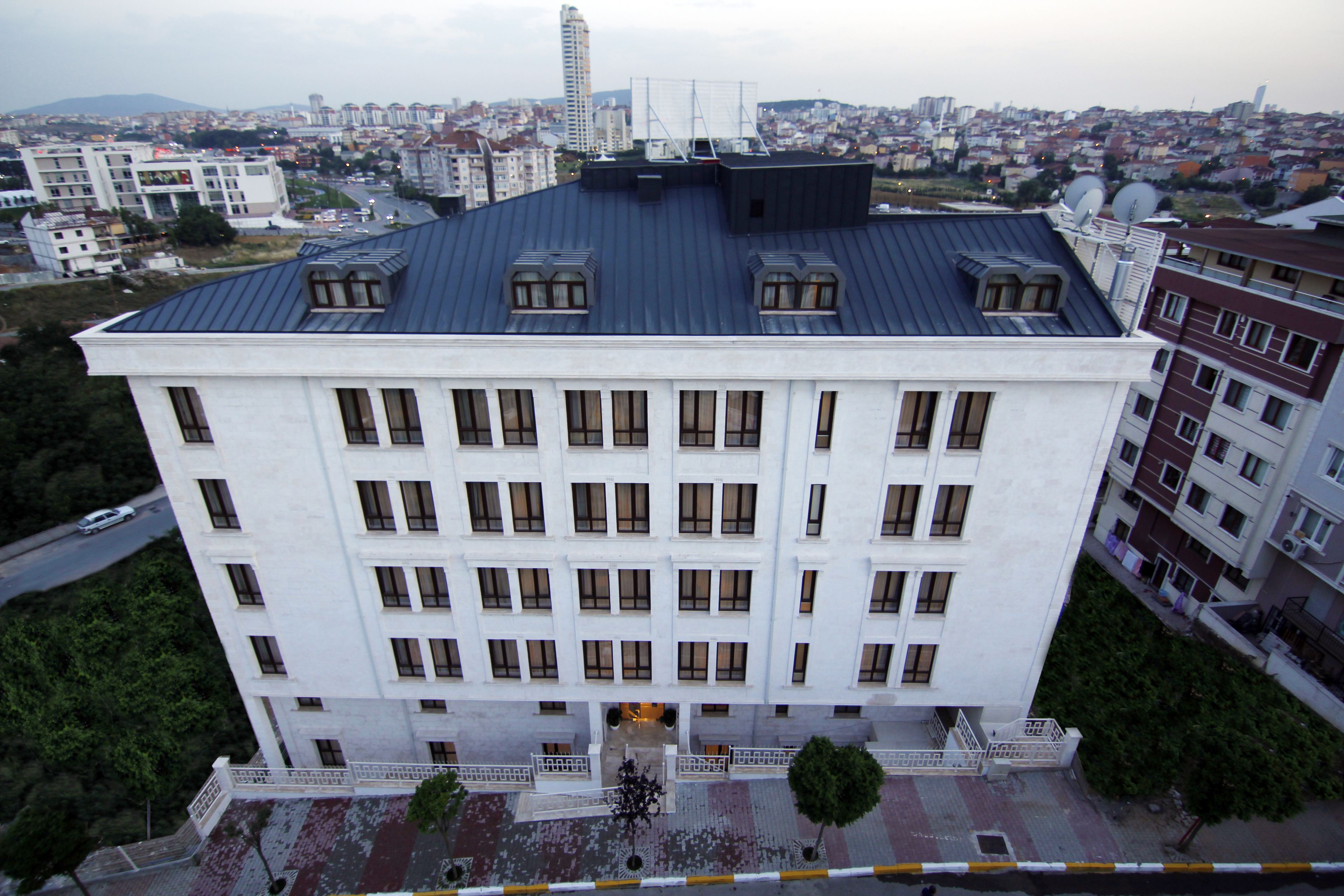 Un edificio de varios pisos con techo plano, numerosas ventanas y una entrada central con un pequeño patio.