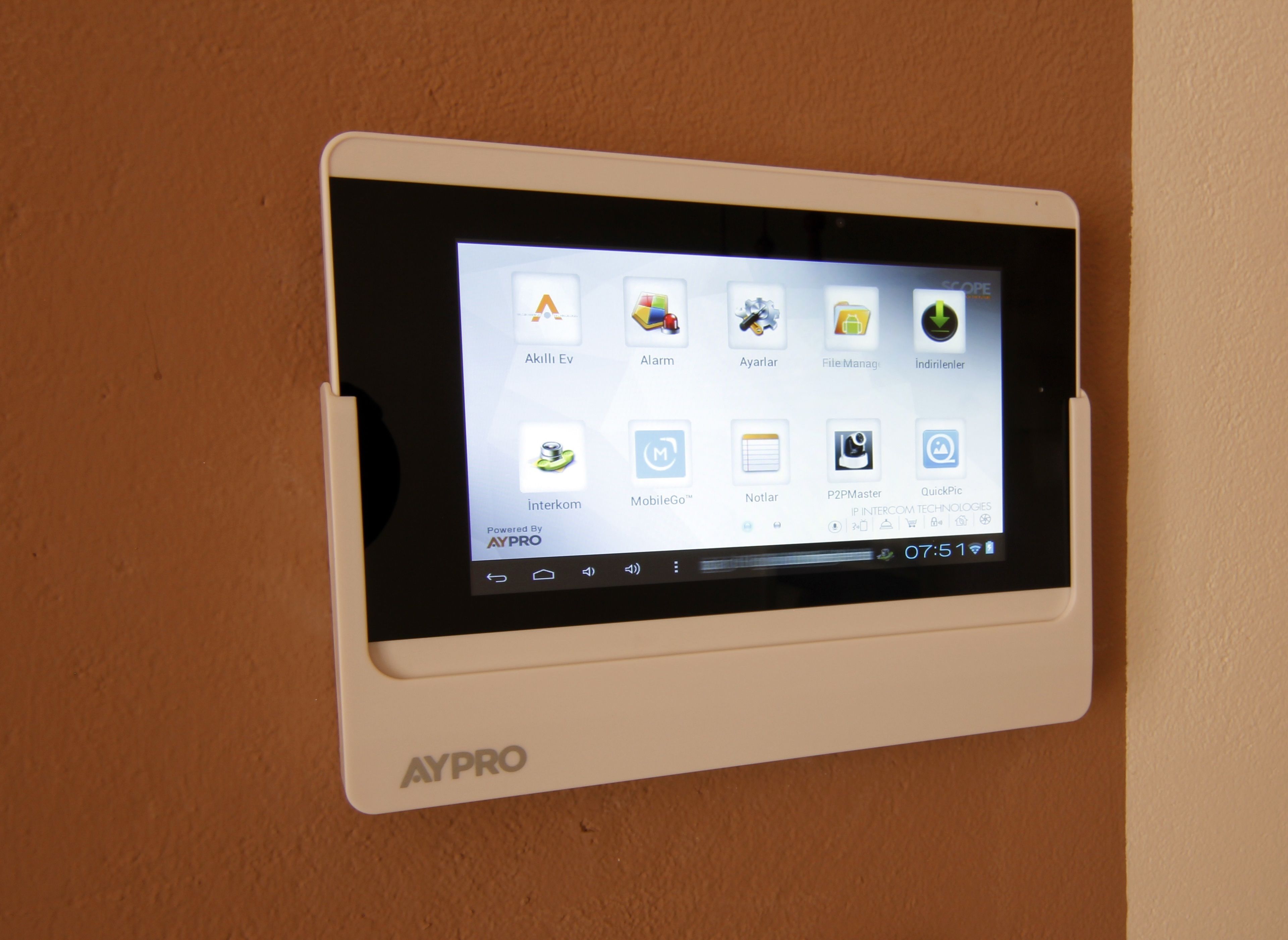 Un dispositivo montado en la pared con una pantalla que muestra varios iconos de aplicaciones, incluyendo 'Akulli Ev', 'Alarm', 'Ayarlar', 'FileManag', 'indilnelis', 'interkom', 'MobileGo', 'Notlar', 'P2PMaster', y 'QuickPic'.