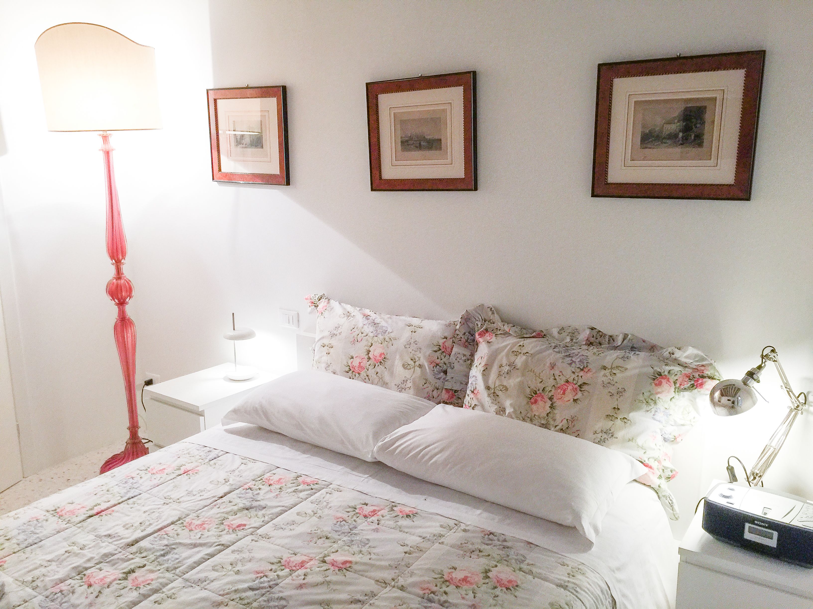 A bedroom with a bed, a bedside lamp, a nightstand, and three framed pictures on the wall.