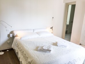 A neatly made bed with a white quilt and pillows, a bedside lamp, and a folded towel on the bed. - Cà Farnese (Venice)
