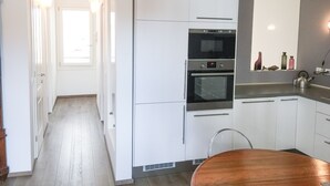 A modern kitchen with white cabinets, a built-in oven, and a dining area with a wooden table. - Cà Farnese (Venice)