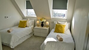 Un dormitorio con dos camas individuales, una mesita de noche con lámparas, un jarrón con flores y una ventana con vistas al exterior.