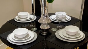 Una mesa de comedor dispuesta con platos, tazones y copas de vino blancos, con un jarrón de flores blancas en el centro.
