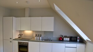 Una cocina moderna con armarios blancos, un horno de acero inoxidable, un microondas y un hervidor sobre la encimera.