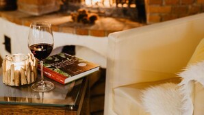 A cozy room with a brick fireplace, a glass table with a book and a glass of wine, and a white sofa.