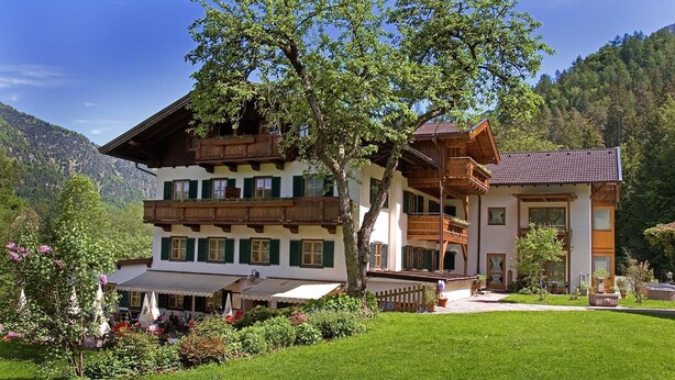 A traditional multi-story building with balconies, surrounded by lush greenery and a mountainous backdrop.
