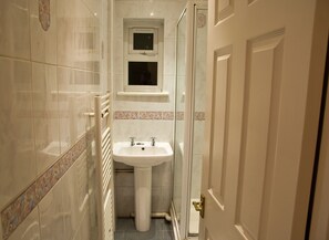 A narrow bathroom with a pedestal sink, a small window, and a door. - Icon Hutton Apartment (Brentwood)