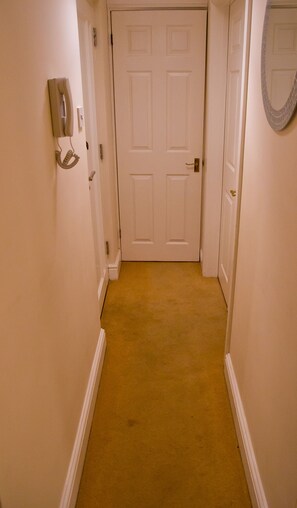 A narrow hallway with a beige carpet, white walls, and a closed white door at the end. - Icon Hutton Apartment (Brentwood)