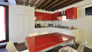 Una cucina moderna con mobili rossi, un tavolo in vetro e sedie bianche.