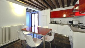 Una cucina moderna con mobili bianchi, uno schienale rosso e un soffitto in legno. È presente un tavolo da pranzo con sedie bianche.