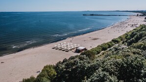 A beach with umbrellas, a small building, and a pier in the distance. - Hotel Sopot (Sopot)