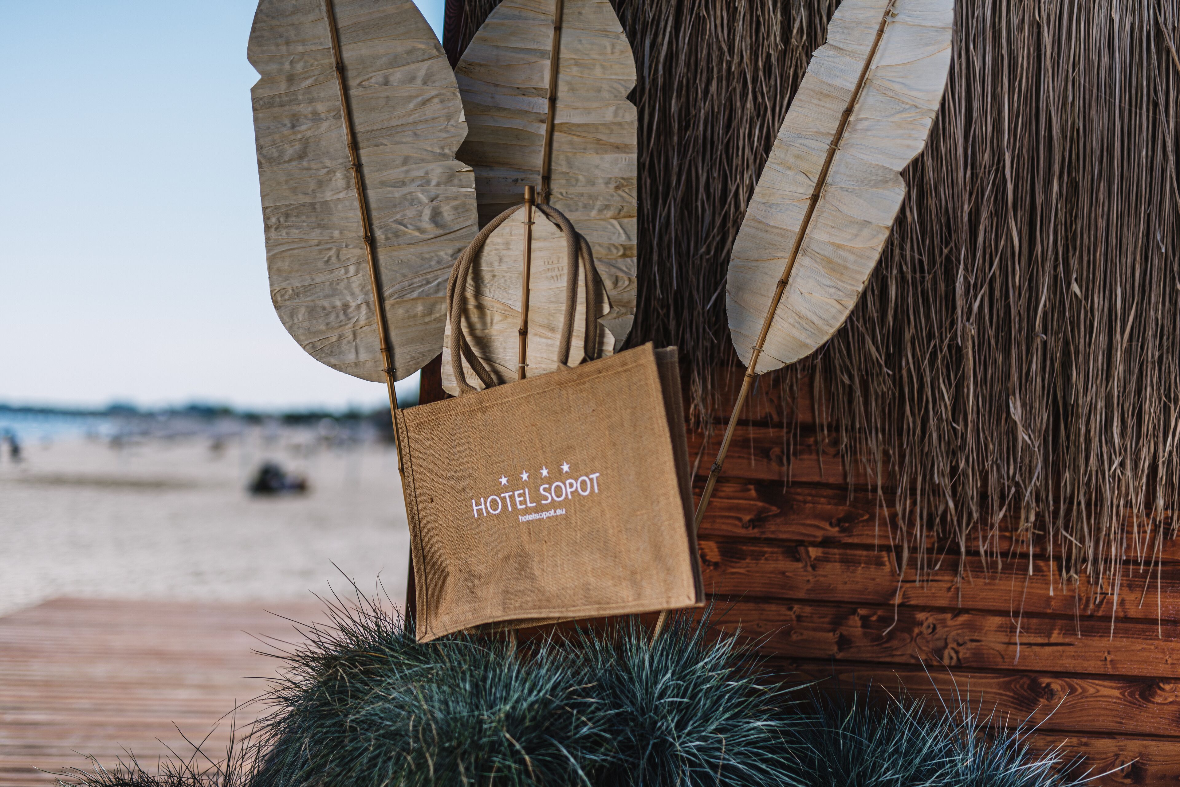 A beachside wooden structure with a beach view, a brown paper bag with "HOTEL SOPOT" text, and pine branches.