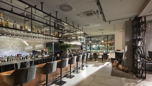 A modern bar area with multiple stools, shelves of bottles, and glasses. - Hotel Sopot (Sopot)