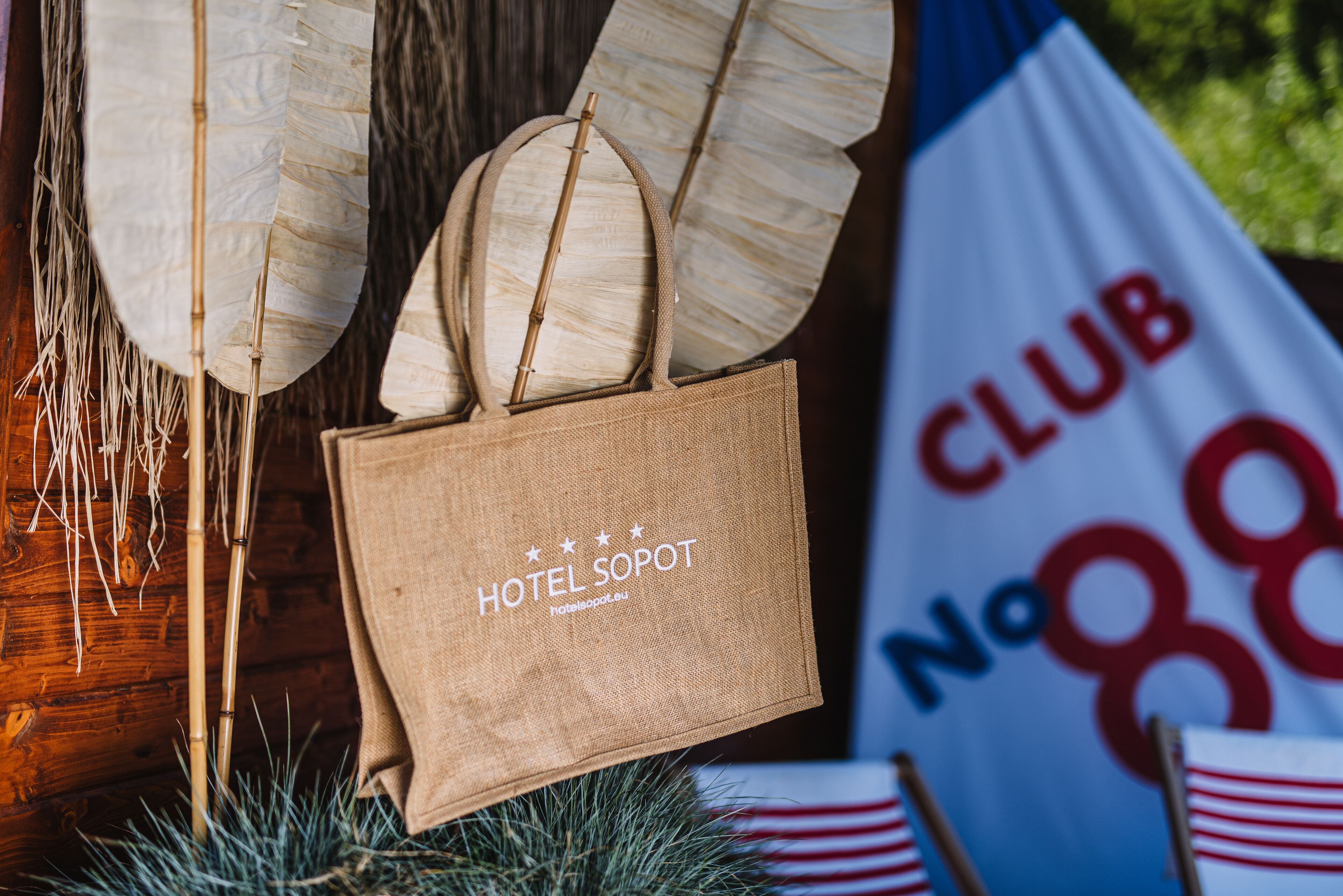 A burlap tote bag with "HOTEL SOPOT" text, a wooden backdrop, and a "CLUB No 88" sign.