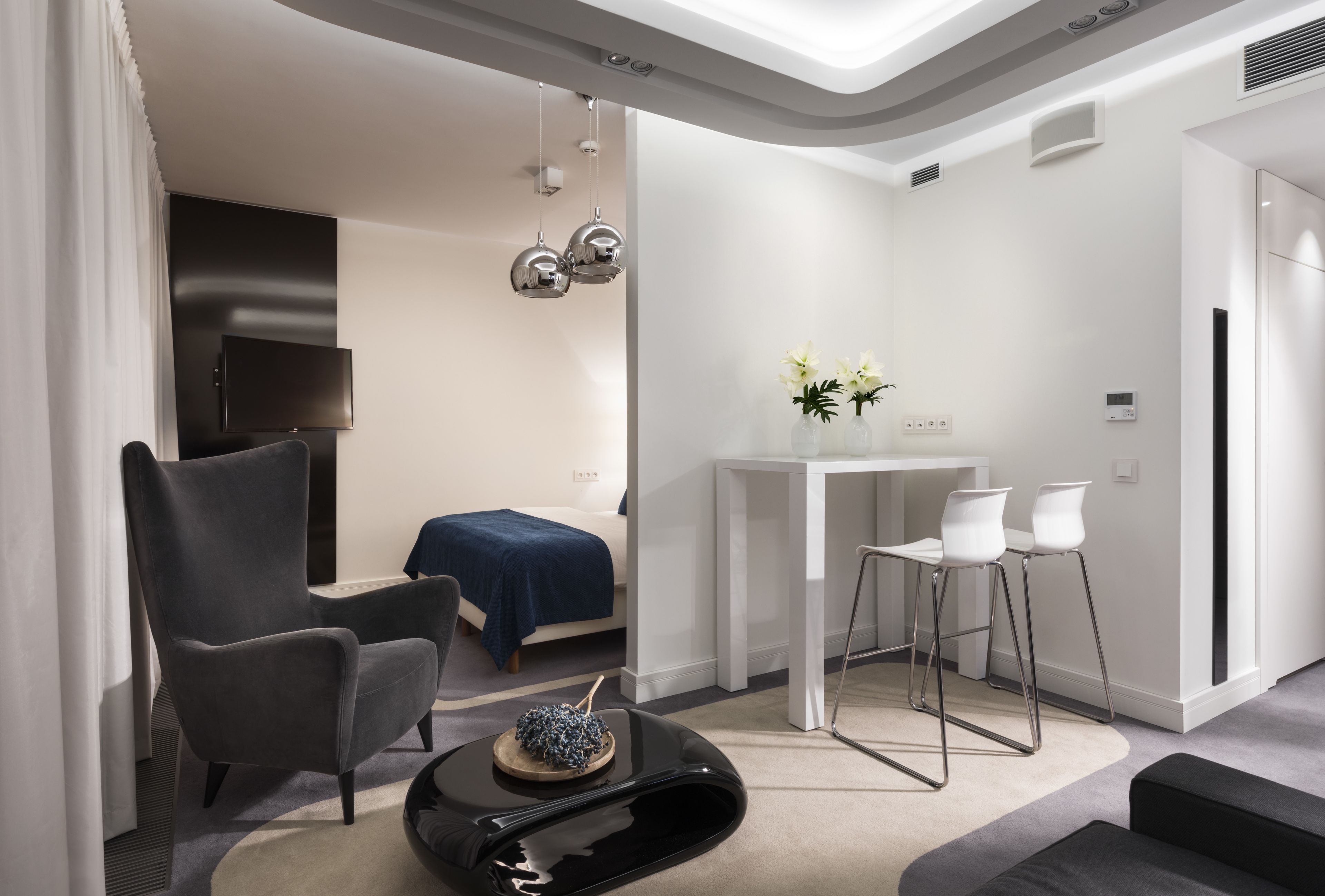 A modern living room with a large armchair, a small table with a decorative bowl, and a white dining area with two chairs.