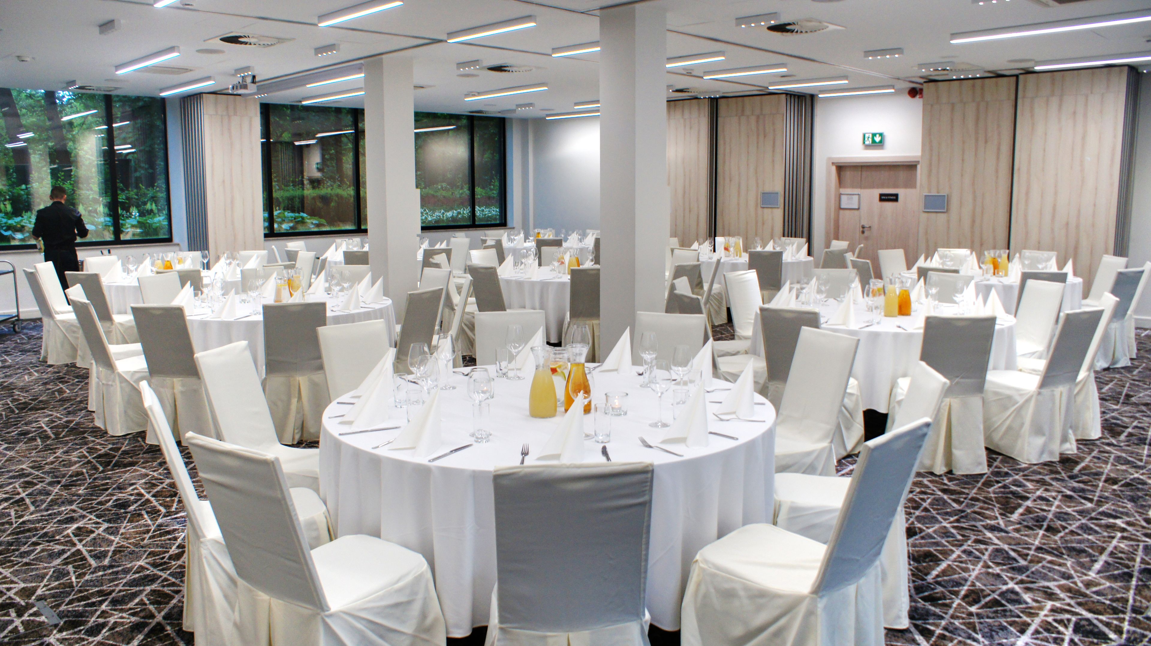Un salón de conferencias con mesas redondas, sillas blancas y suelo alfombrado.