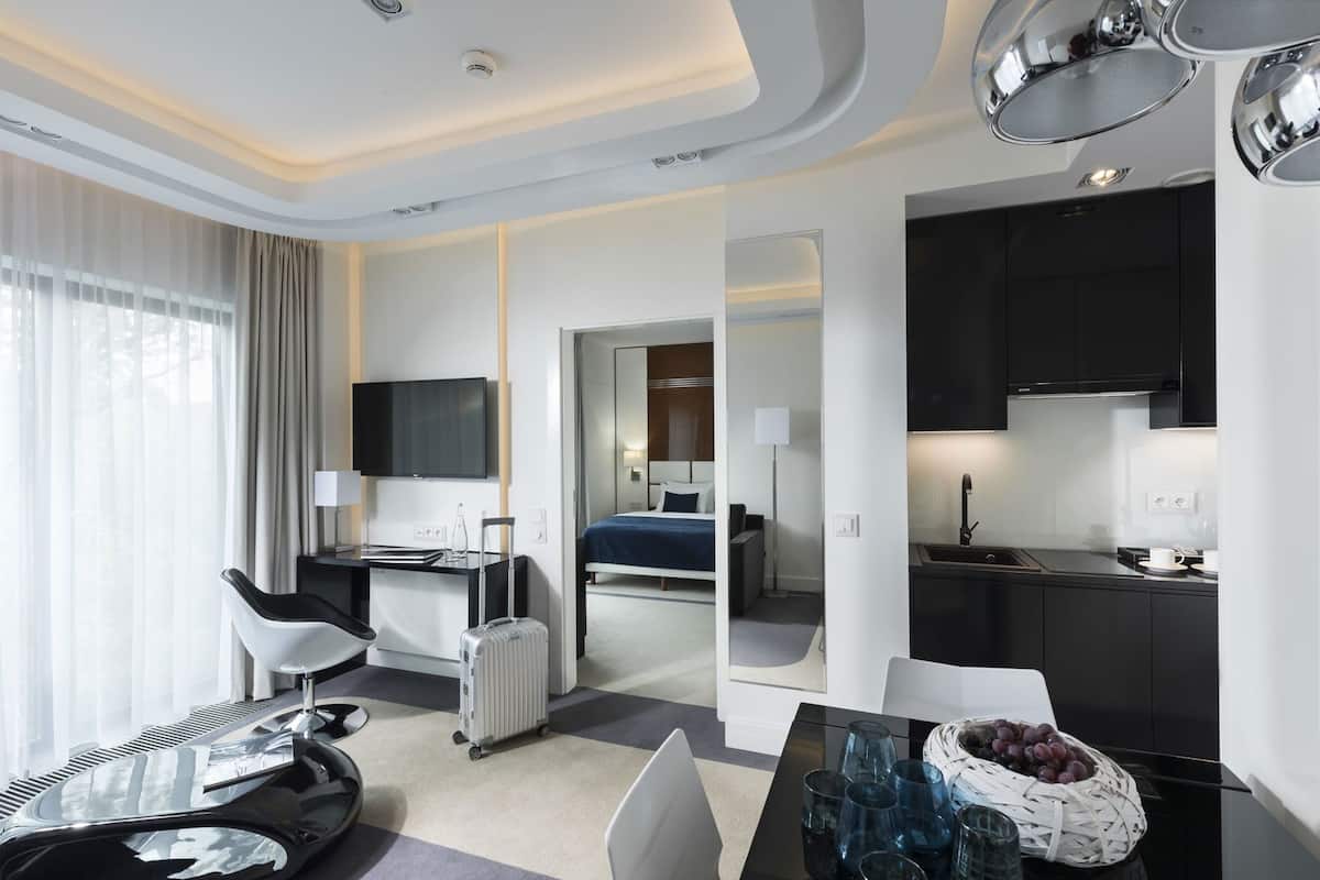 Ein modernes Hotelzimmer mit Schreibtisch, Stuhl, Bett, Küchenzeile und einer Essecke mit Tisch und Stühlen.