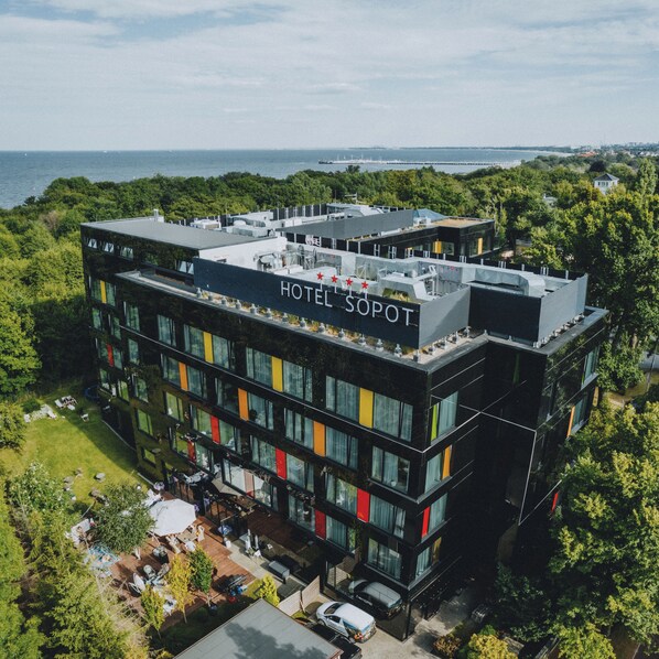 Um hotel moderno com terraço no telhado, vários andares e vista para o mar.